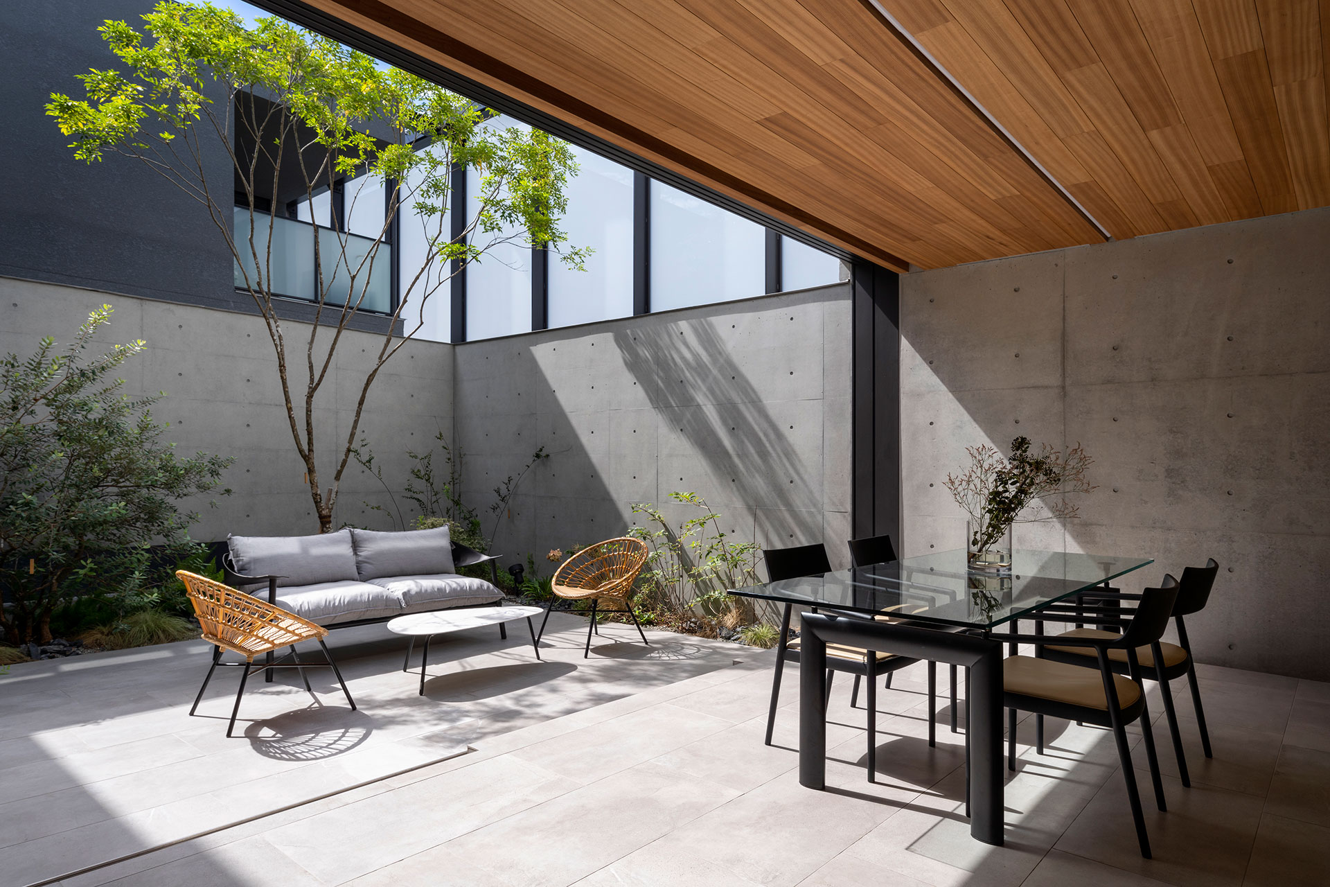 関西の建築家・真銅祥一朗設計の中庭のある家のアウターリビング コンクリート打ち放しとガラススクリーンの塀、タイル貼りの床、板貼りの天井で構成される。